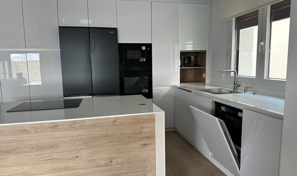Cocina blanca y madera, isla central, electrodomésticos negros integrados.