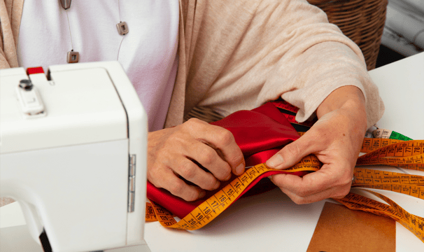 Couturière mesurant un tissu rouge à la main avec un ruban de mesure, illustrant la création