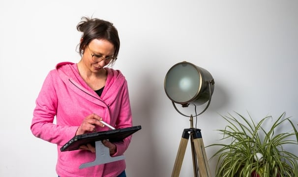 a woman in a pink jacket and jeans standing in front of a lamp