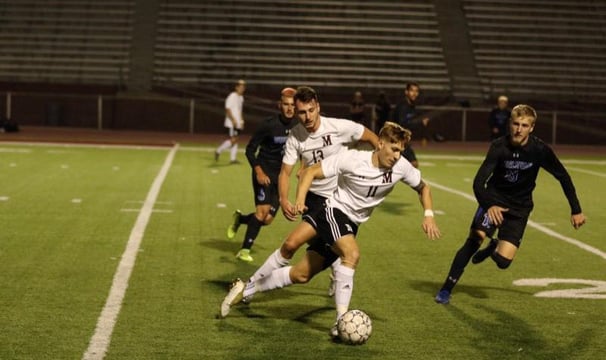 College soccer players competing on a field, one dribbling the ball