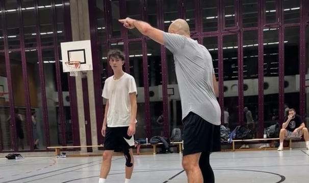 alt="Basketballtrainer gibt Anweisungen an Jugendspieler im Training."