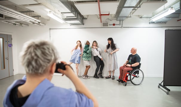 Four standing people of various ethnicities and a manual wheelchair user being photographed