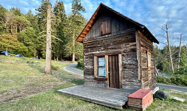A historic, rough-hewn cabin on the grass.