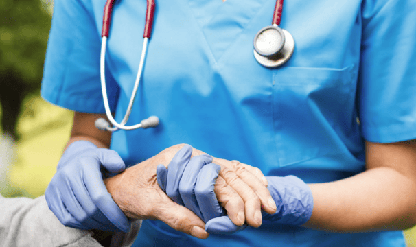 Nurse holding elderly hand, symbolizing compassionate medical decisions in estate planning.