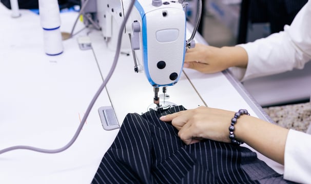 Señora cosiendo con una maquina de coser una tela azul con rayas blancas