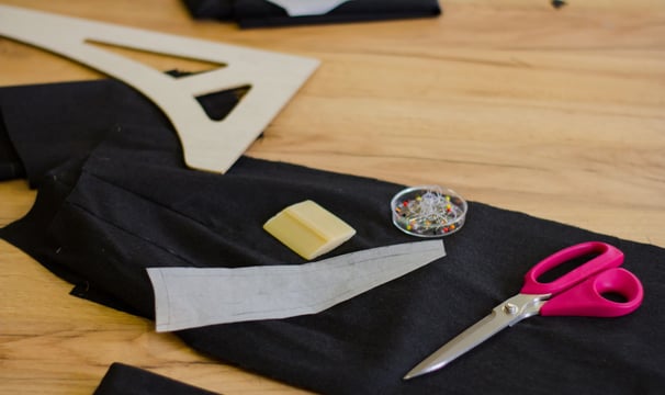 Trozo de tela, patron de ropa, unas tijeras y unos alfileres sobre una mesa de madera