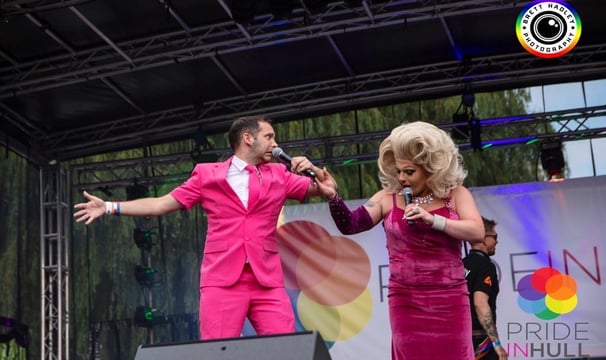 Alex in a pink suit hosting Pride in Hull. A drag queen in pink is holding his hand
