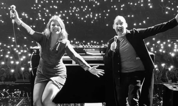 Alex Duffy and Ellie Brennan on stage in black and white in front of bright white lights from phones
