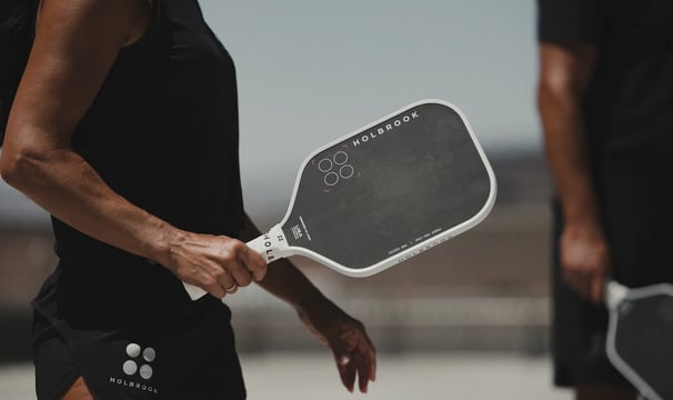 Close-up of athlete holding a black Holbrook pickleball paddle during outdoor match.
