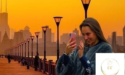 photographie corrigée, femme souriante regardant son portable sur un fond de lumière dorée et sur un bord de fleuve calme