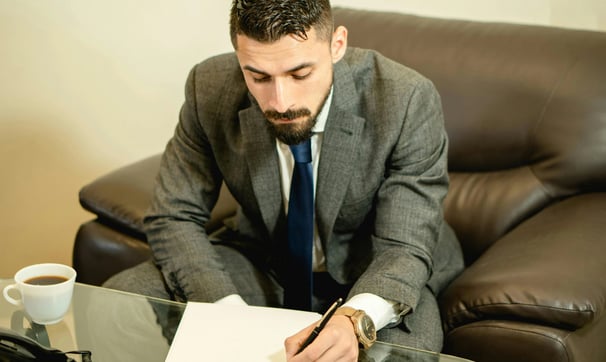 un hombre con traje y corbata escribe en un papel