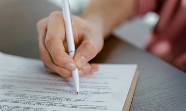 una persona que sostiene un bolígrafo y escribe en un papel