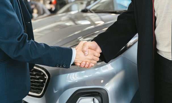 un hombre y una mujer se dan la mano delante de un coche