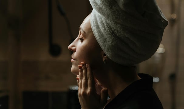 A woman in a robe studying her face in the mirror while her hair is wrapped in a towel.