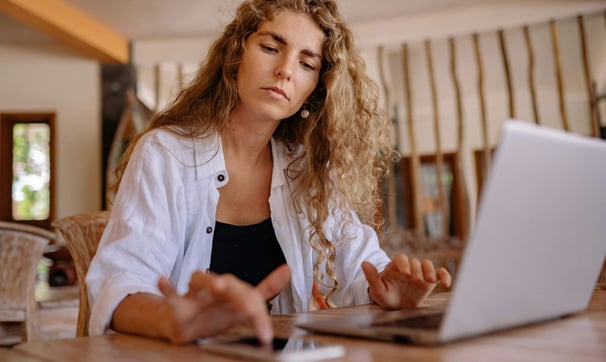 A stressed woman using a calculator and a laptop