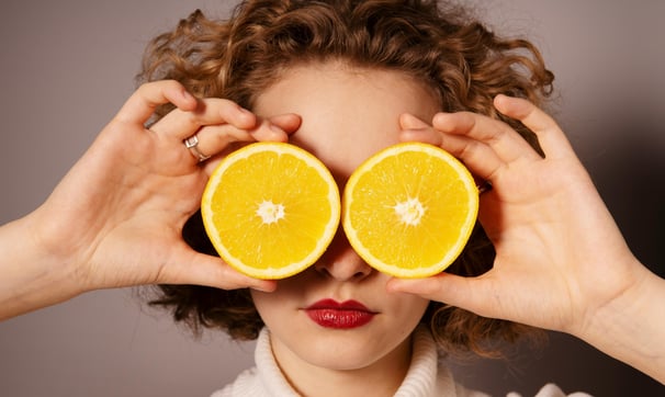 Woman holding up 2 orange slices to her face to cover her eyes.