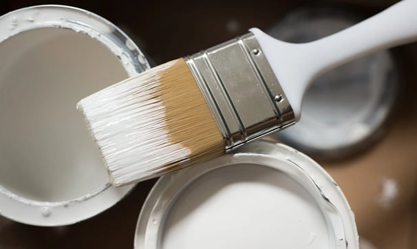 se está utilizando una brocha para pintar un bote de pintura blanca