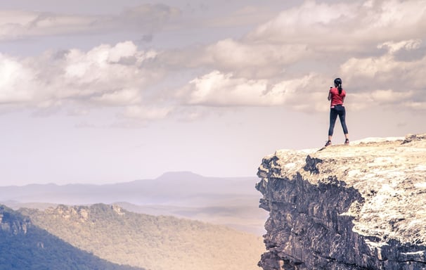a person standing confidently at the top of a rock and overlooking a vast landscape - Holistic Health Company