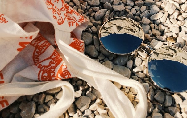 Foto de óculos de sol e bolsa de tecido sob pedras pequenas.