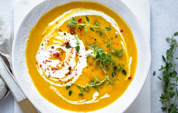 anti-inflammatory vegetable soup in white bowl with herbs and pomegranate seeds