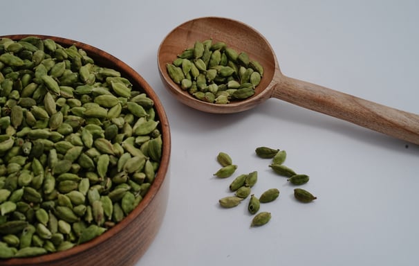 Green Cardamom placed in Wooden Tumbler and a wooden spoon