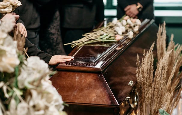 hand touching the dark brown stained coffin decorated by dried flowers