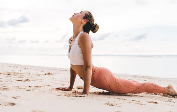A woman practicing yoga on the beach - Holistic Health Company