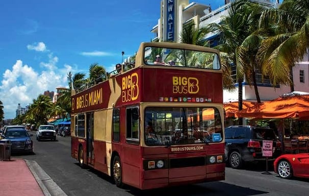 a red double decker bus driving down ocean drive