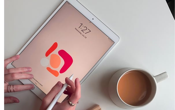 Person doing design work on a tablet, cup of tea next.  Represents branding and design.
