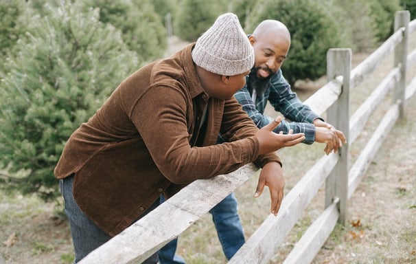 A father and son leaning with their elbows on a wooden fence having a conversation