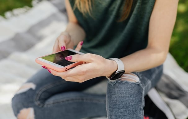 A teenage girl wearing ripped jeans sitting on a blanket looking at her phone