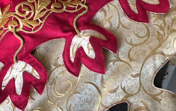 Photo de détails d'une tenue rouge et dorée avec des motifs dits de feuilles de chêne