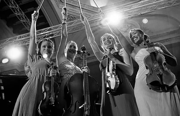 a group of women in dresses and hats holding violin instruments