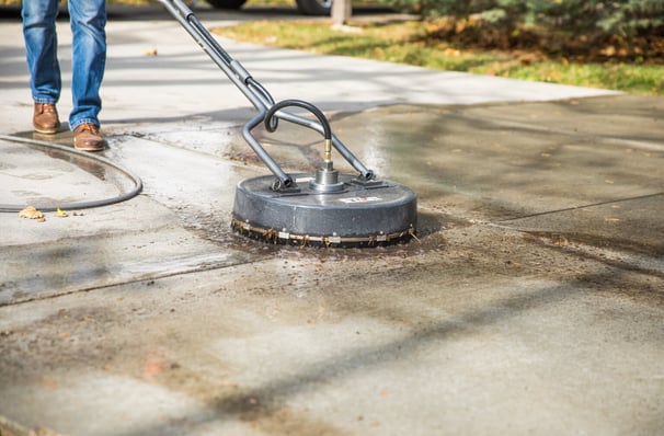 Pressure washing services worker using a surface cleaner to clean concrete