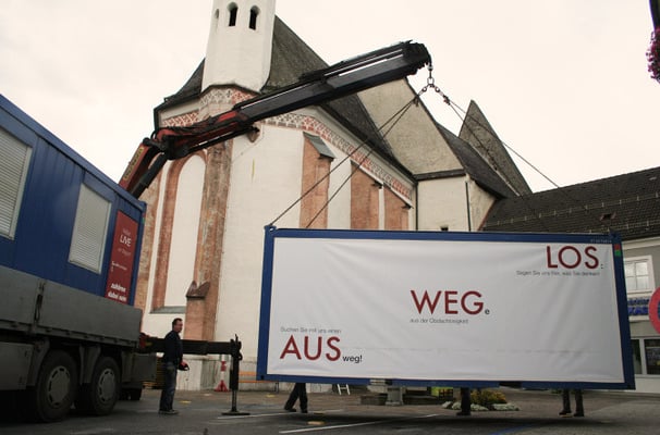 Kran bei der Aufstellung des Ausstellungscontainers "Aus weg los!" auf einem Dorfplatz.