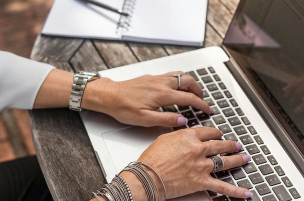 Frau tippt auf einen Laptop an einem Tisch draußen. Homeoffice und Karriere