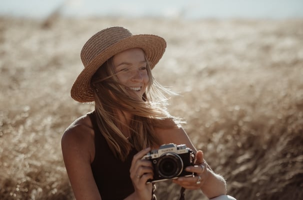 Portrait of a woman in a hat, she is holding a camera and smiling