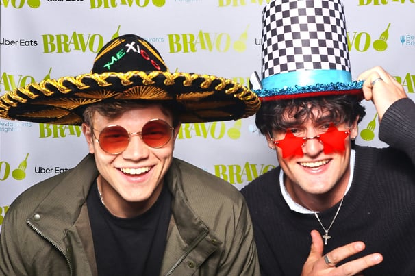Two young men smile for a photo in Get The Picture photo booth wearing fun hats and glasses at awards party