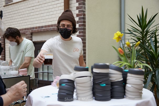 Ein Barista mit einer schwarzen Maske, der einen Kaffee serviert.