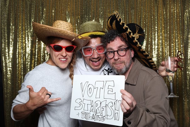 Three guests excitedly pose for a photograph in the get the picture vintage photo booth hire UK Brighton with stylish hats