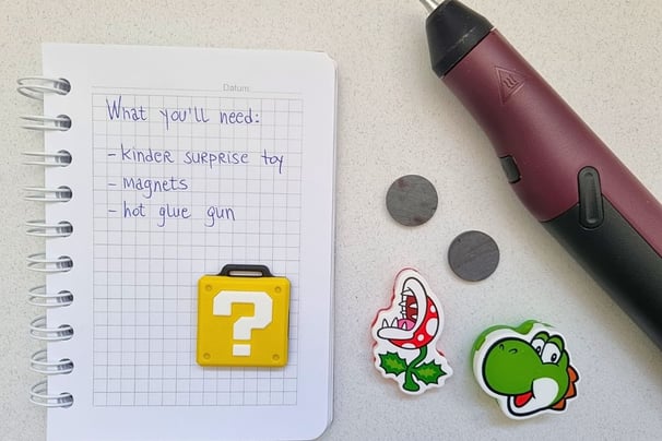 A notepad with a list of DIY materials, including a Kinder Surprise toy, magnets, and a hot glue gun