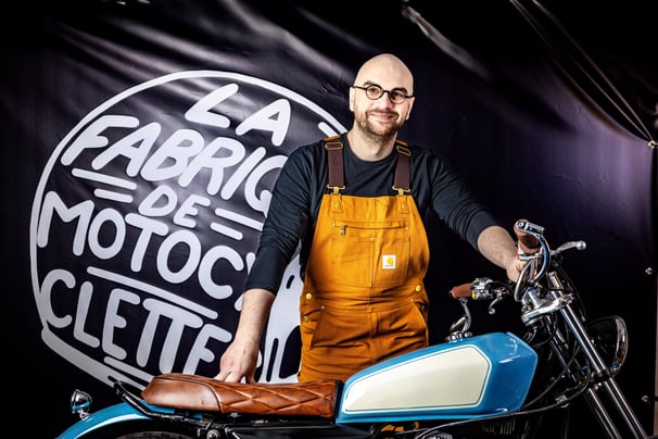 Homme barbu à lunettes en salopette jaune posant avec sa moto