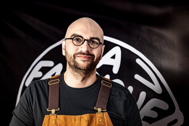 Homme avec une barbe et des lunettes posant devant une banderolle noire