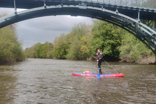 a women standing on a paddle board on the river severn under a bridge, 