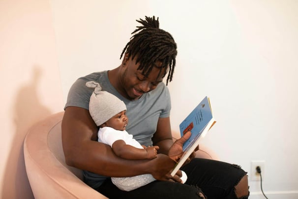 A young father reading a children's picture book to a child.