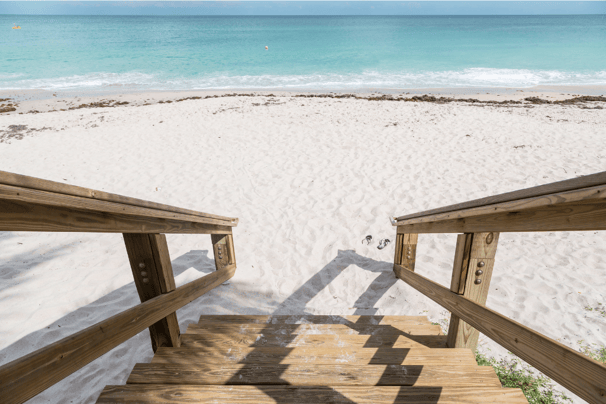 Escalier en bois face à une plage de sable blanc et vue sur la mer