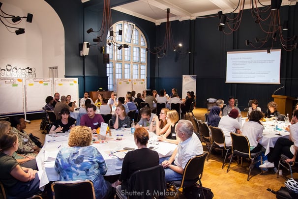 Mehrere runde Tische mit Workshop-Teilnehmern bei Refugio in Berlin.