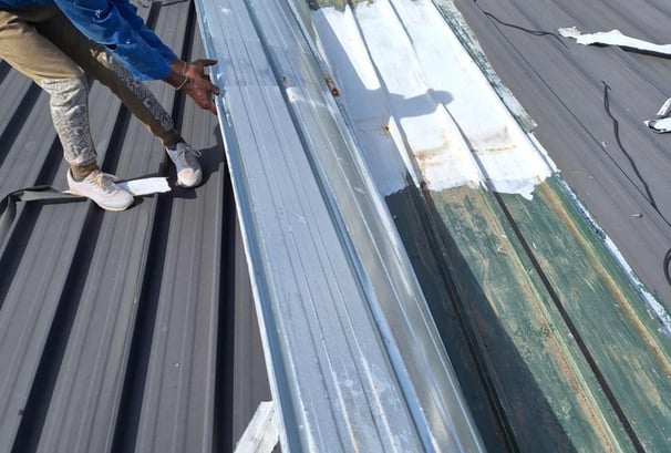 Roof with widespread storm damage, showing loose and bent metal sheets.