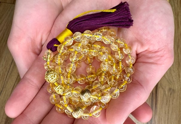 A handcrafted mala made with Citrine and Gold with purple tassel