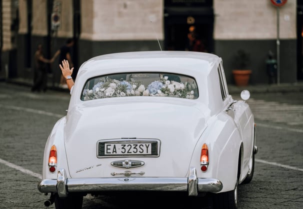 mano che saluta dello sposo, mentre va via con una macchina d'epoca